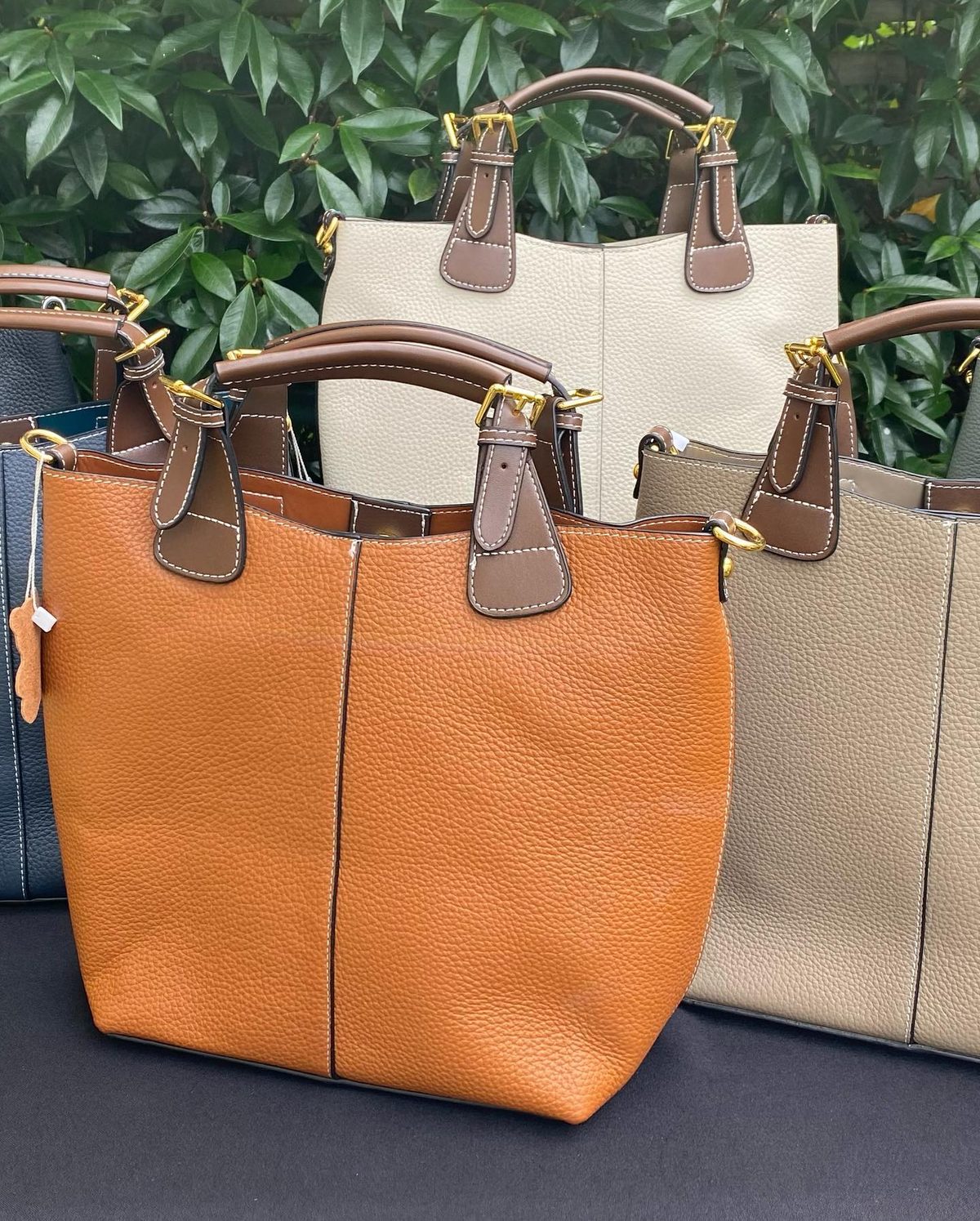 Three pebbled leather bucket totes in tan, cream and taupe with buckled handles